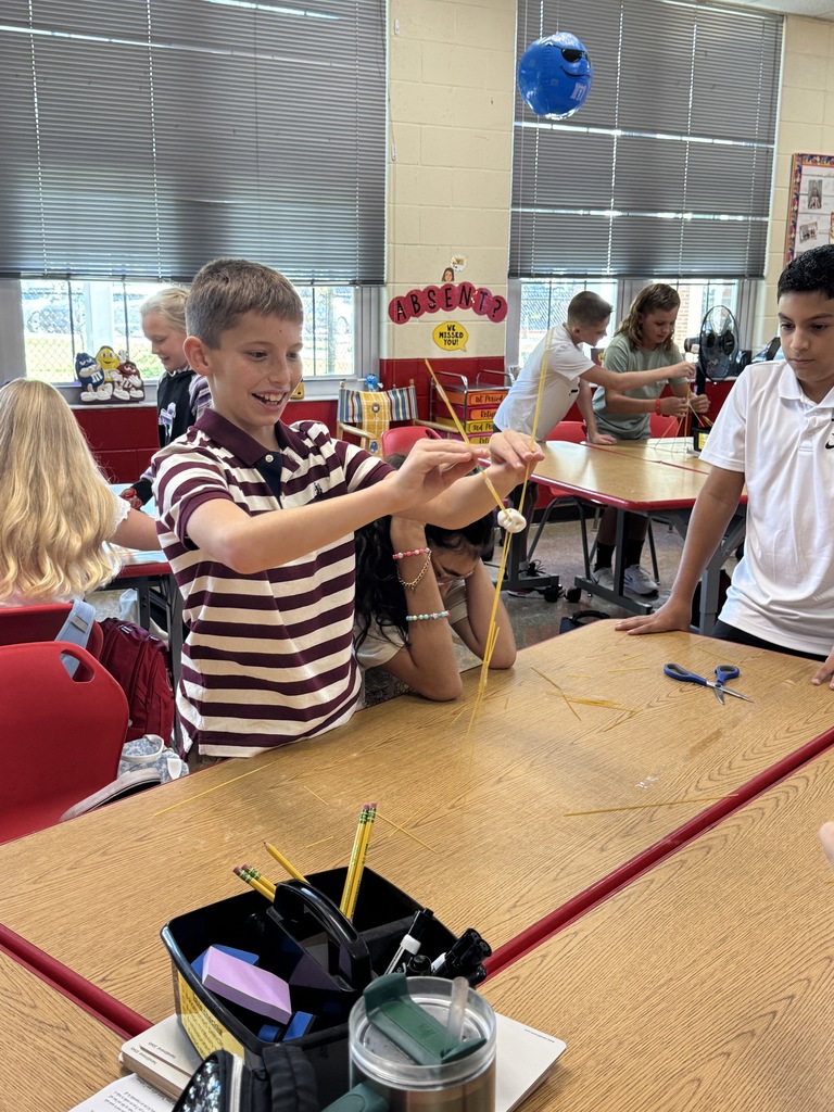 Elementary students in a classroom building tall structures with spaghetti noodles and marshmallows, smiling and collaborating.