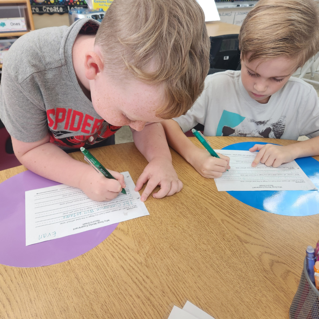 Two students focus on filling out a worksheet, collaborating during their science activity at a classroom table.
