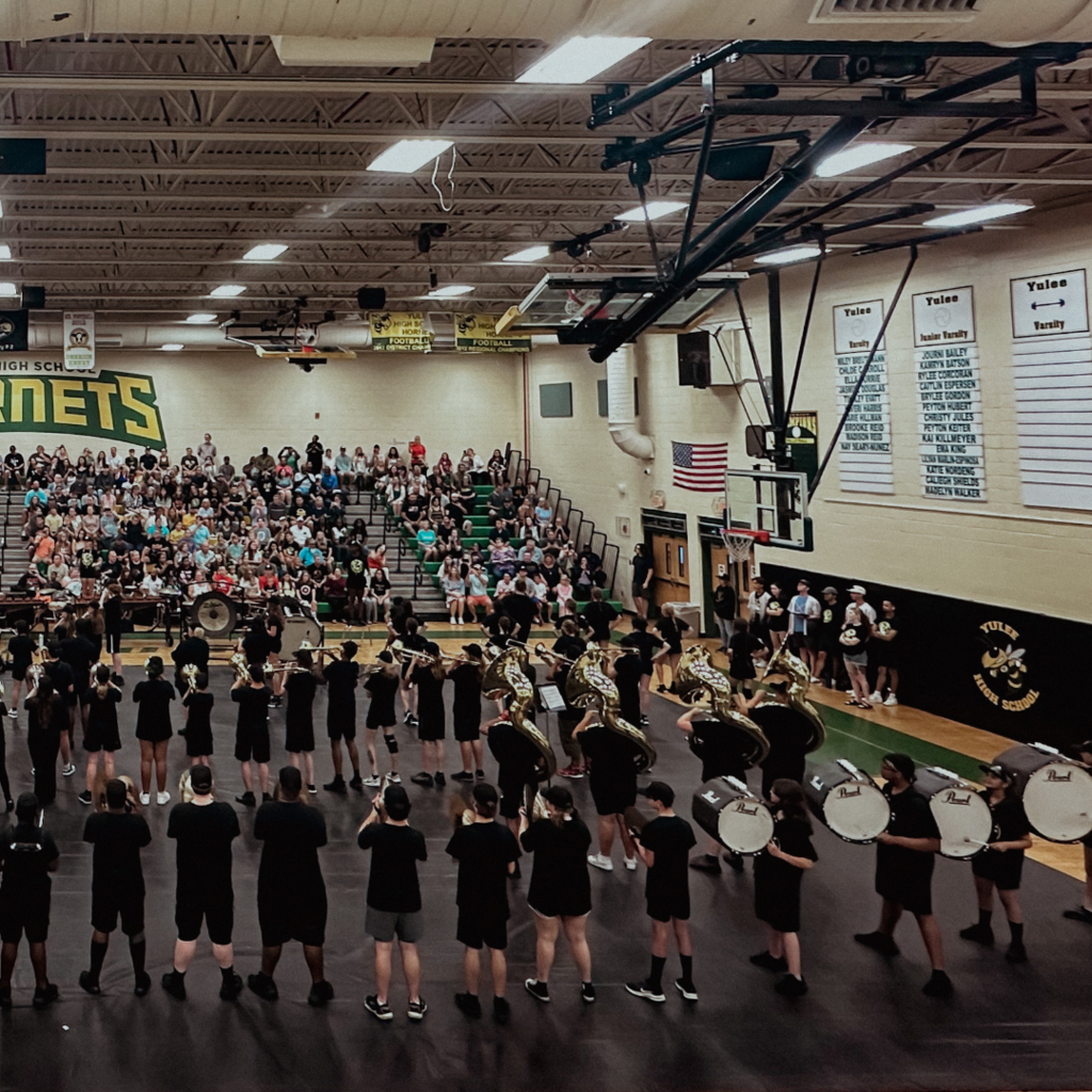 The Yulee High School marching band performs in the school gym as a large crowd of families and supporters watch from the bleachers.