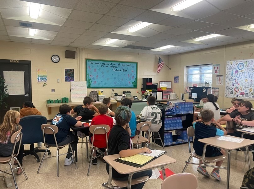 A classroom of sixth grade students seated at desks in groups, facing the teacher’s area.