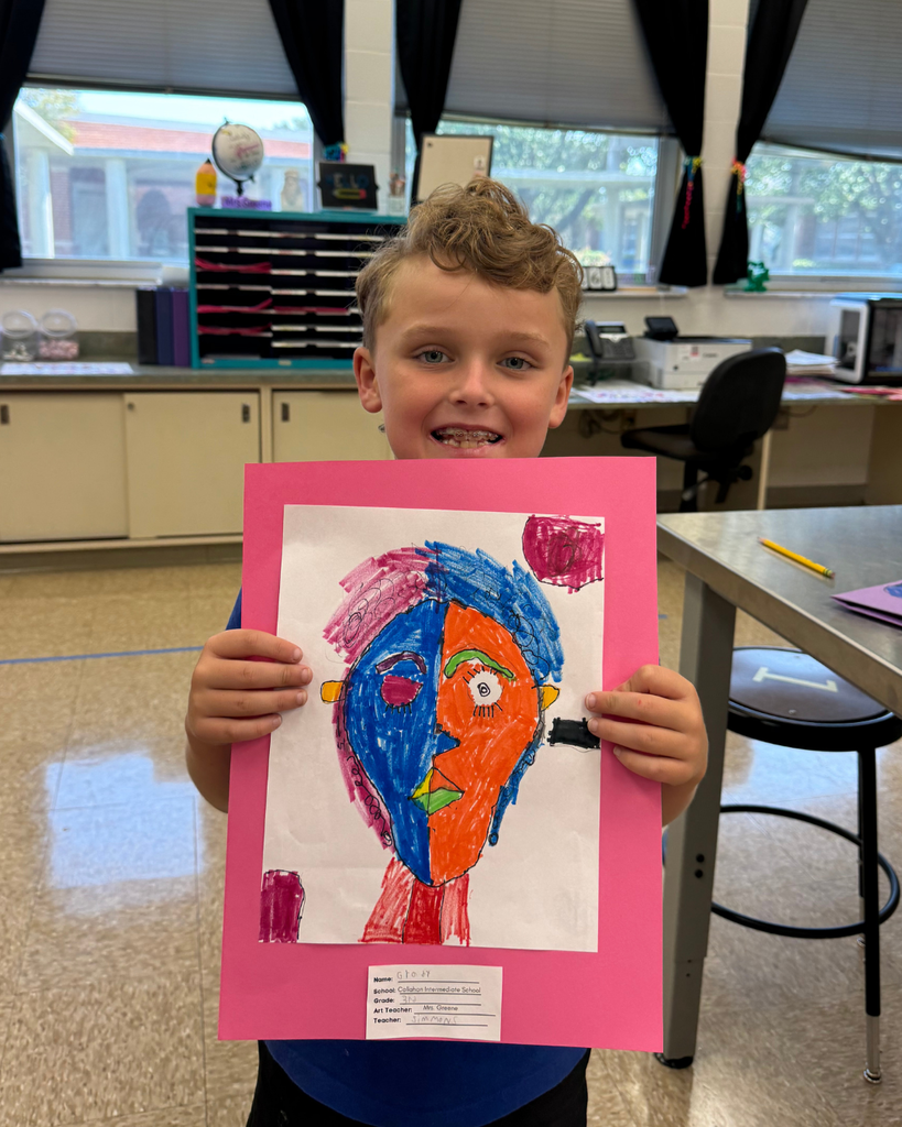 A student holds a Cubism-inspired self-portrait, filled with bold colors and fragmented shapes in orange, green, purple, and black, mounted on pink paper.