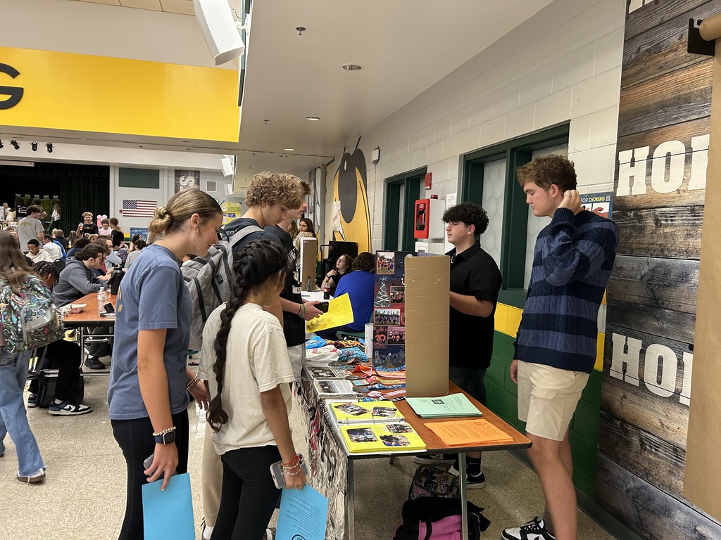 Students stop at a recruitment table for the Marathon High Running Club during Club Rush. They look at the display board, medals, and flyers while members of the club share information.