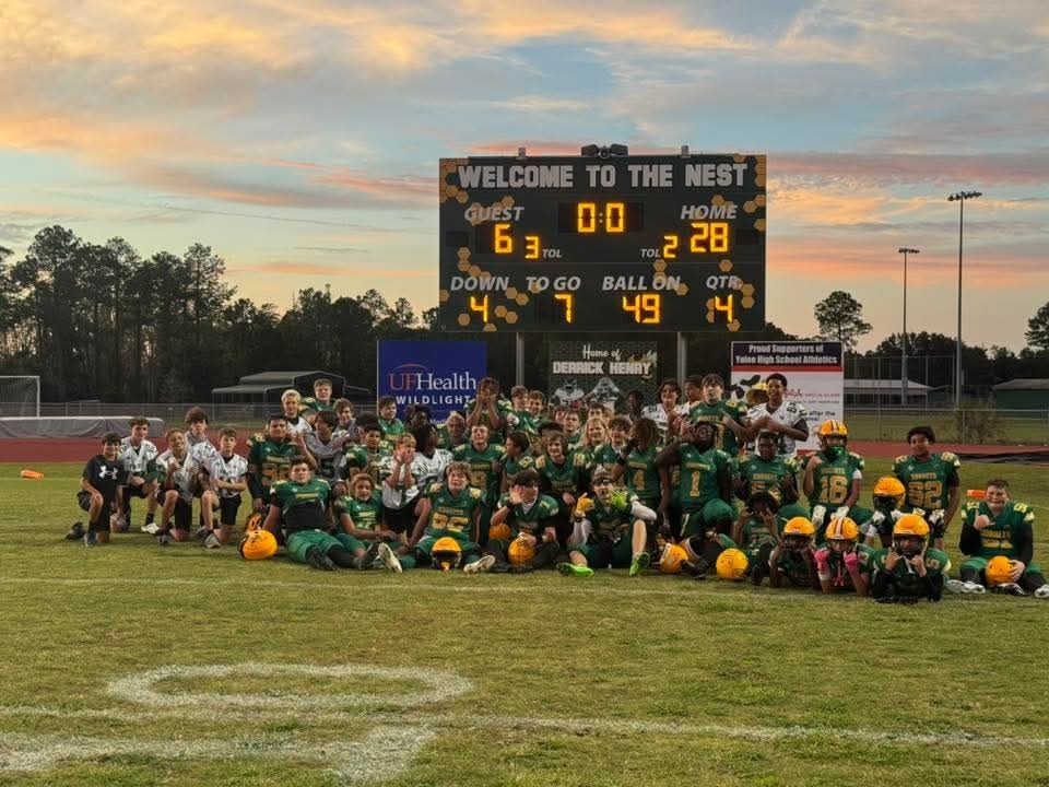 Football players posing in front of the final score board home team 28 guests 6
