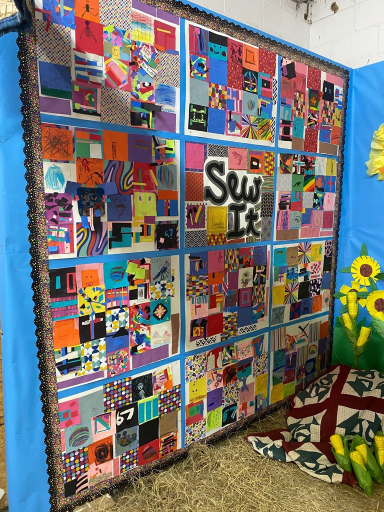 A wall filled with bright patchwork art squares arranged like a quilt, centered around large text reading “Sew It.” The display includes geometric shapes, drawings, and vibrant patterns made by students.