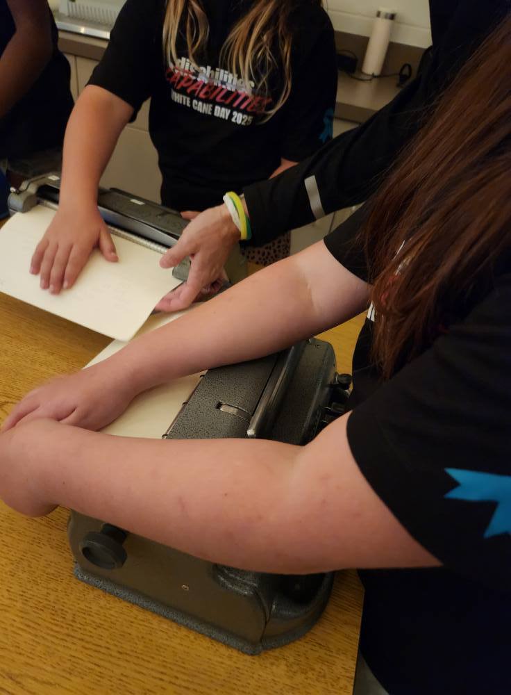 A student uses a braille typewriter to emboss dots onto paper during a hands-on learning activity for White Cane Day.