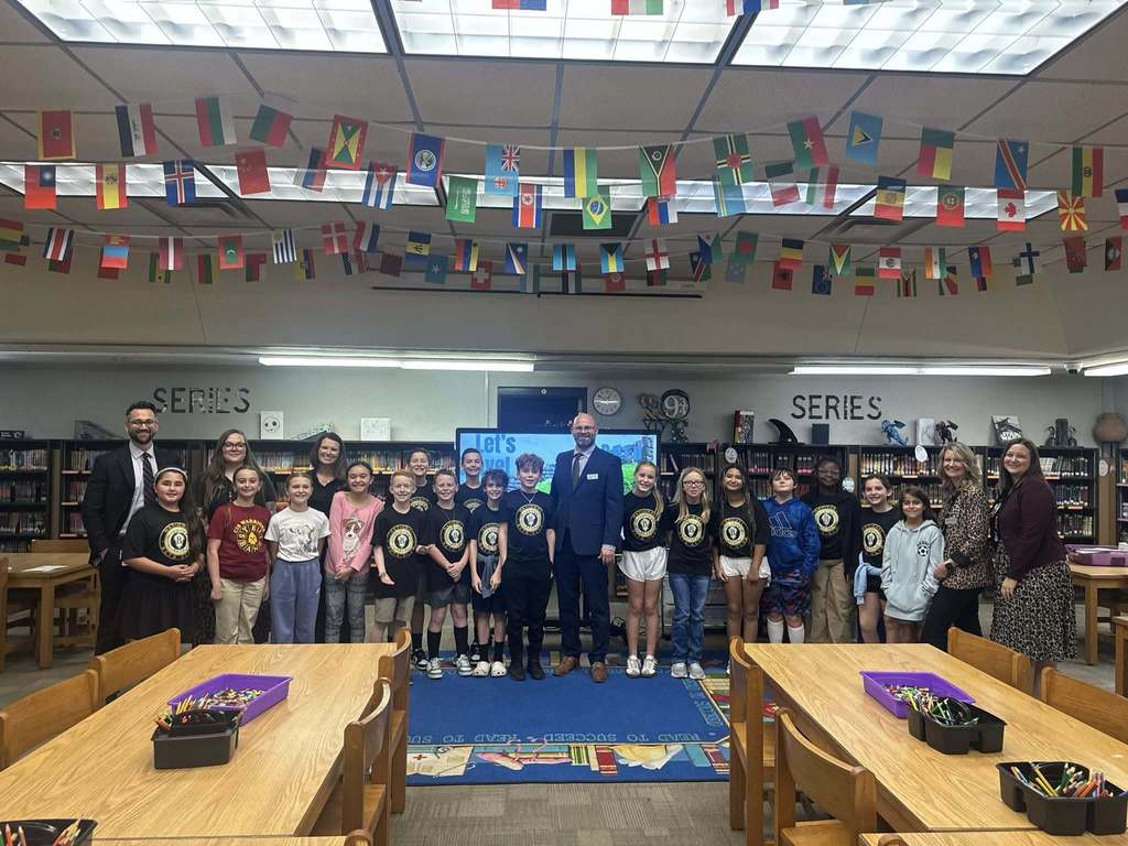 A group of students and staff pose together in the school library at Callahan Intermediate School, with bookshelves, flags, and a presentation screen visible in the background.