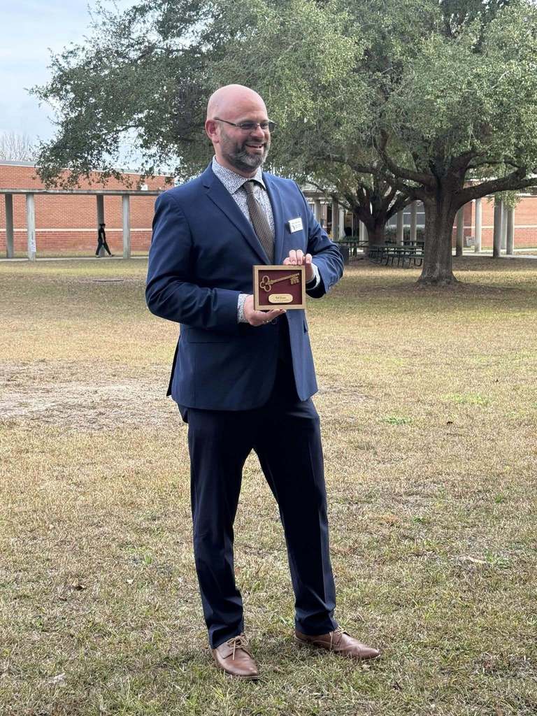 Florida’s Teacher of the Year stands outdoors holding a decorative key presented by Callahan Intermediate School, marking his recognition as an honorary member of the school community.