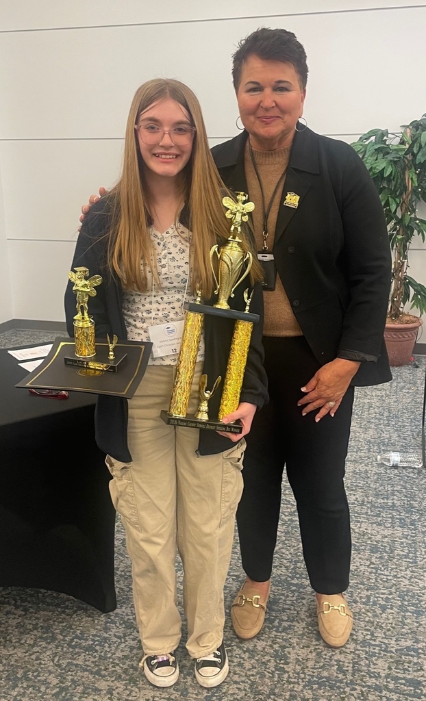 Lacey Solomon, an eighth-grade student from Faith Christian Academy, stands smiling with her first-place spelling bee trophies while posing with Superintendent Dr. Kathy Burns after the Nassau County School District Spelling Bee.