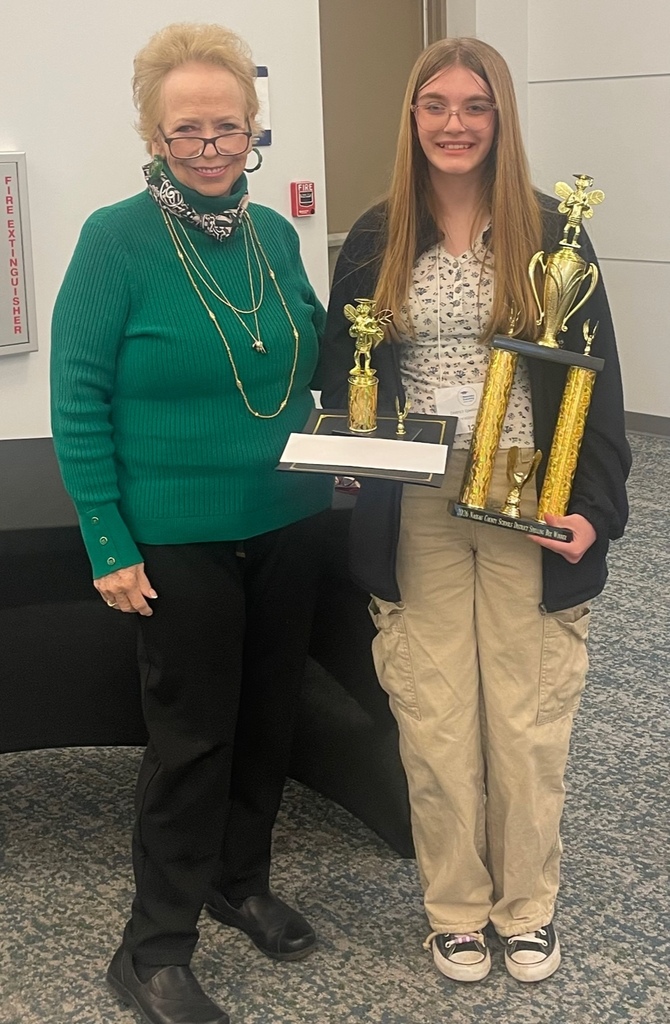 Lacey Solomon, an eighth-grade student from Faith Christian Academy, smiles while holding first-place spelling bee trophies as she poses with Optimist Club representative Jacque Osborne after the Nassau County School District Spelling Bee.
