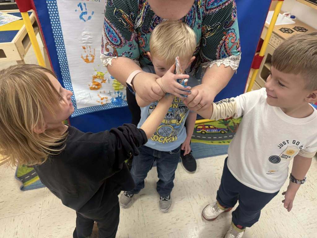 Three Pre-K students and an adult stand together as students press paint-covered hands together during a color-mixing activity in the classroom.