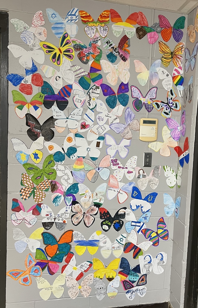 Wall covered with colorful student‑made butterflies featuring Holocaust remembrance messages and symbols.