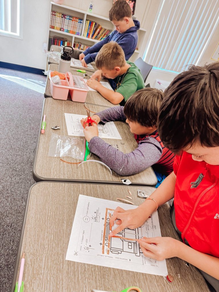Students seated at desks carefully cut and place copper tape on paper circuit templates as part of an electricity lesson.