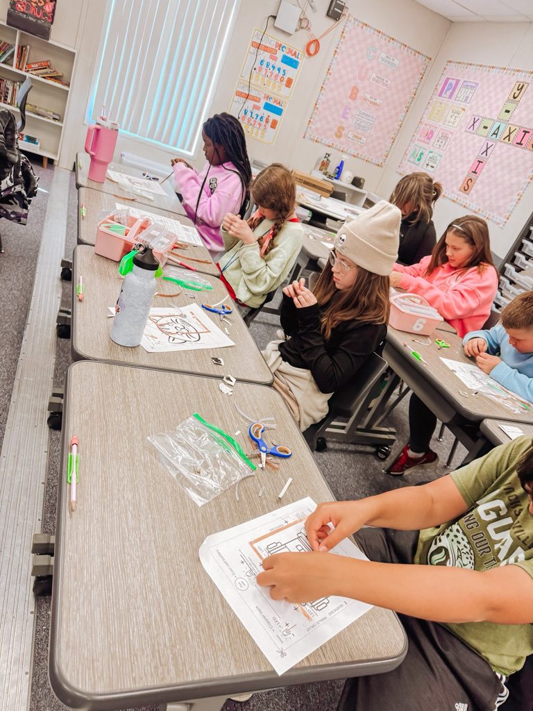 A classroom view shows multiple students working independently on paper circuits using copper tape, scissors, and instructional diagrams.