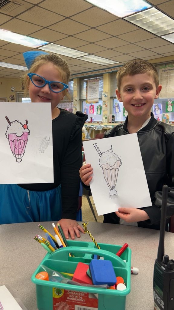 Two students smile while holding drawings of milkshakes they created during a lesson connected to 1950s culture.