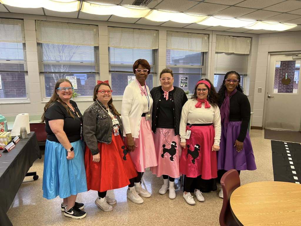 Teachers pose together in a classroom wearing 1950s-style outfits and glasses as part of a themed instructional day.