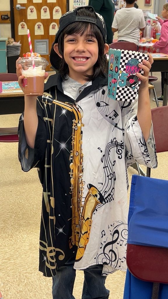 A student smiles while holding a cup and a themed container during the 1950s classroom activity.