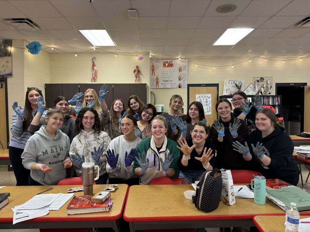 A group of CNA students smile and hold up gloved hands covered with chocolate and strawberry syrup used to simulate germs.