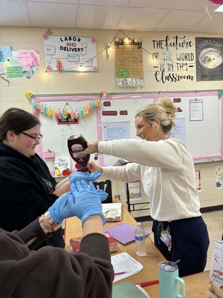 An instructor demonstrates safe glove removal while students observe and participate in the activity