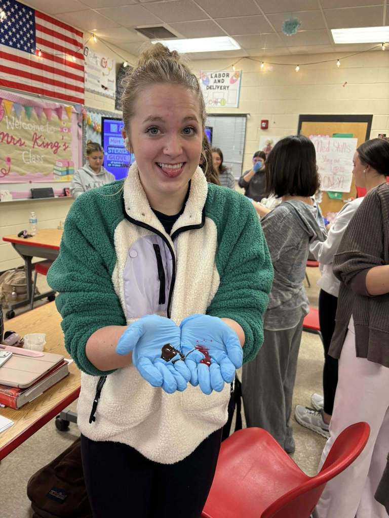 Students wearing gloves extend their hands toward the instructor as part of a guided infection control simulation.