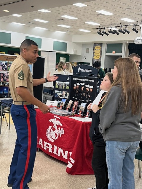 A representative from the United States Marines speaks with students and a family at a military recruitment booth during the district’s College & Career Fair.