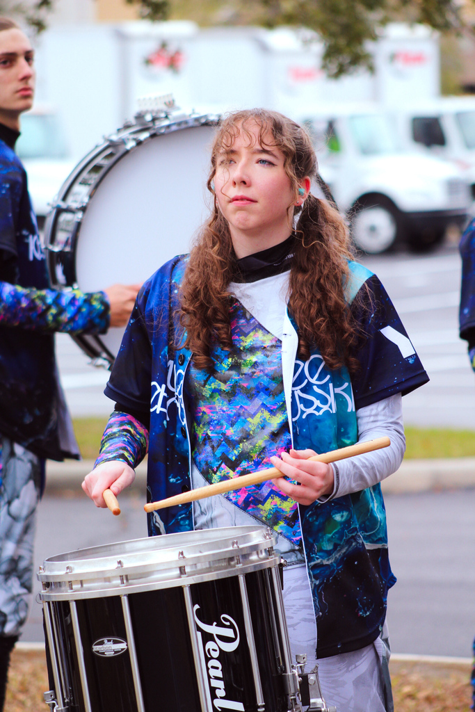 Yulee High School band member wearing teal ear protection plays a snare drum during competition preparation.