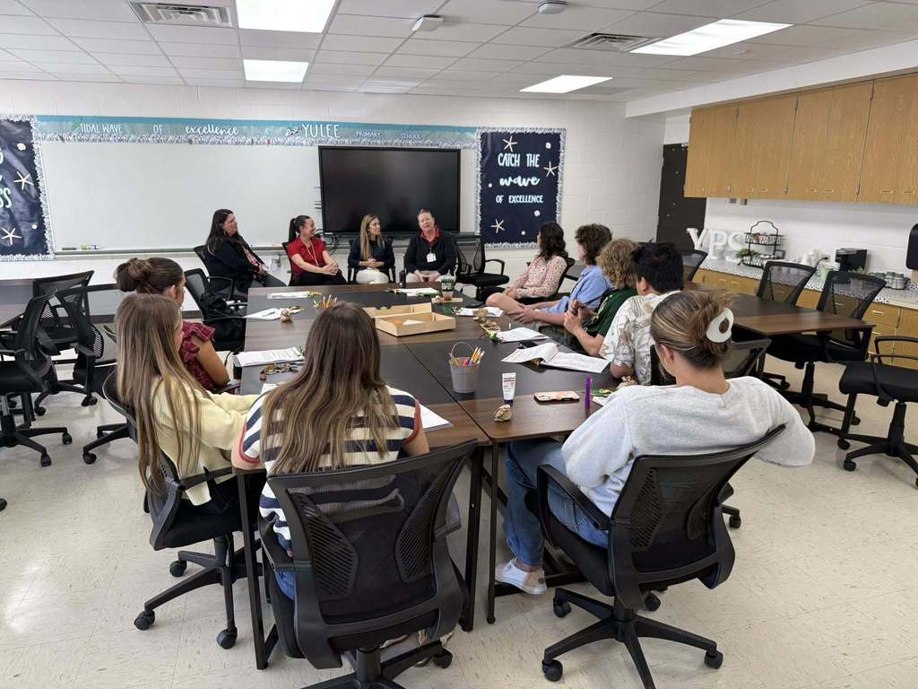 A group of Yulee High School students sit around a conference table at Yulee Primary School participating in a question and answer session with four primary teachers seated at the front of the room.