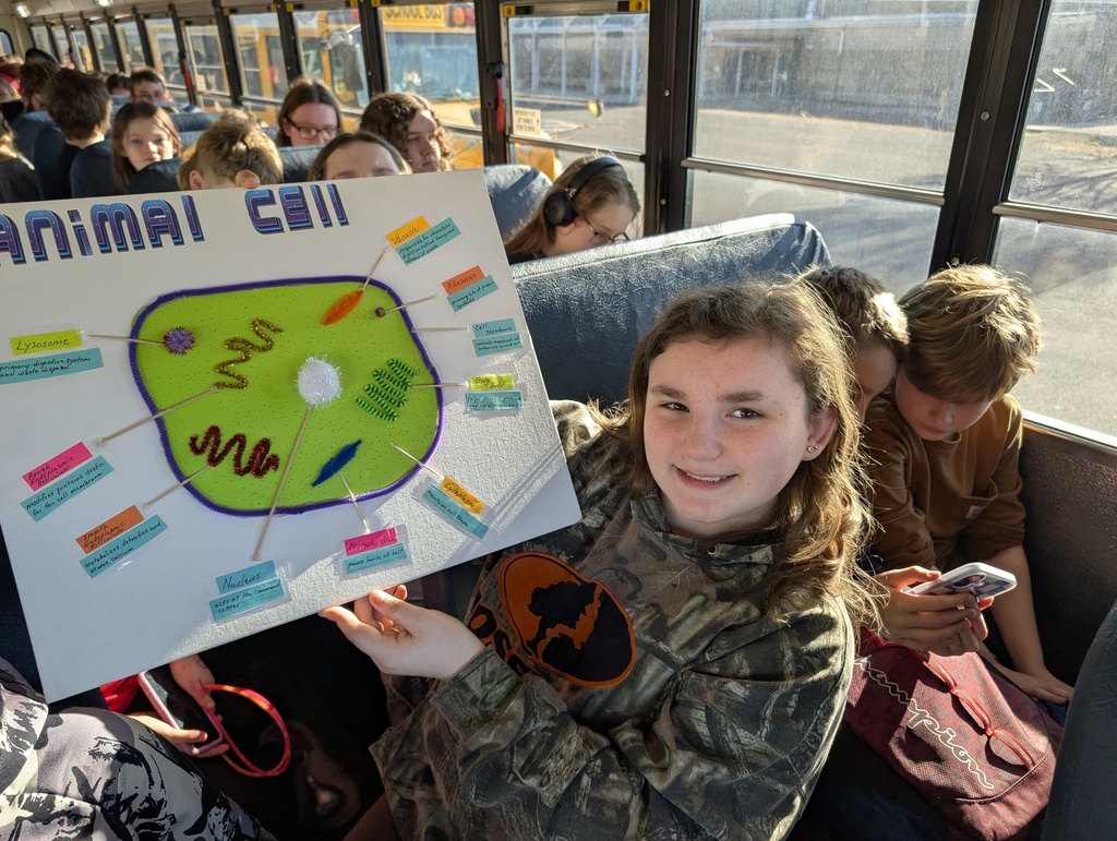 Student holds up their animal cell project on a school bus while smiling. 