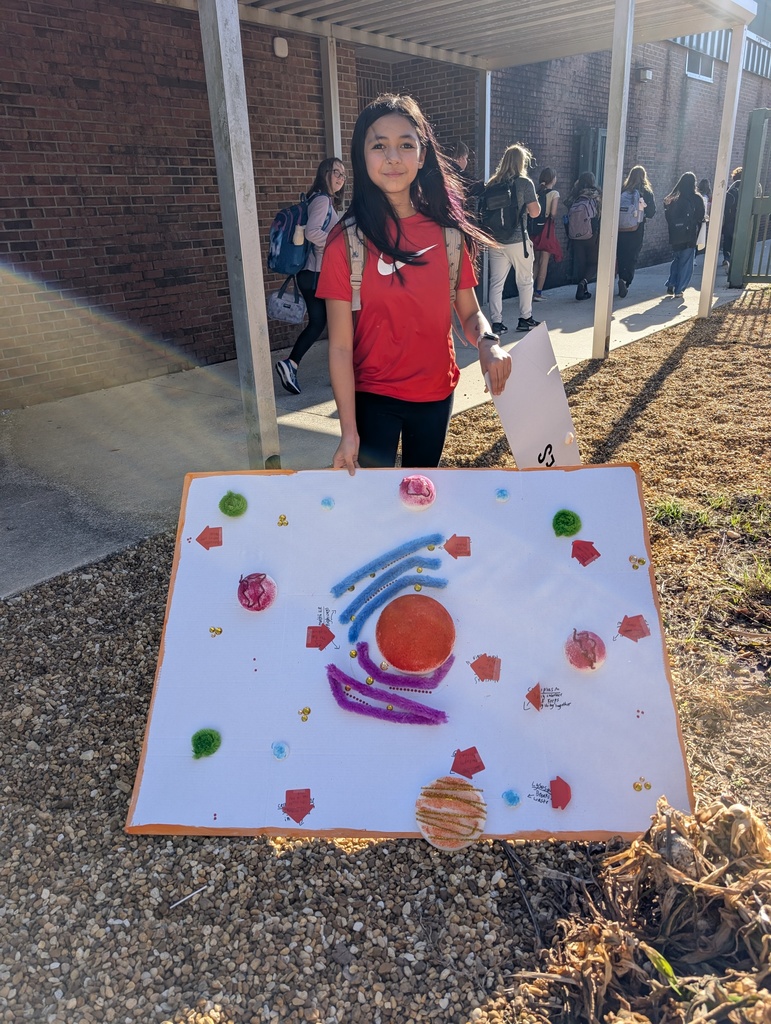 Student shows off her poster of an animal cell next to the school outdoor sidewalk. 