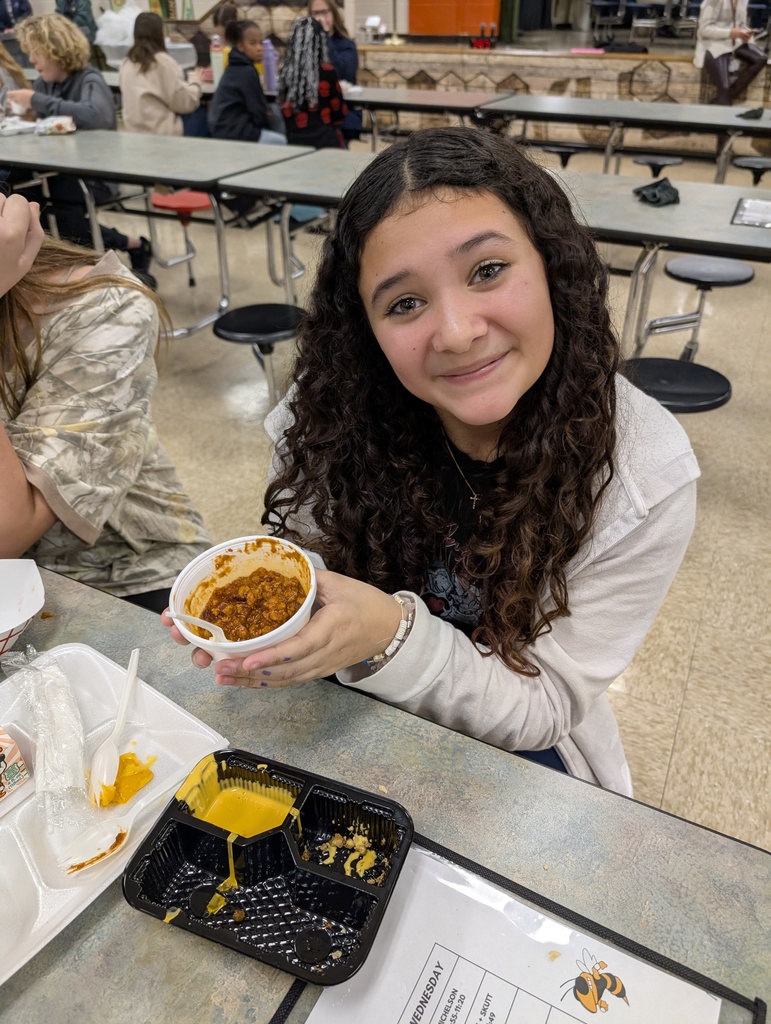 A student smiling while holding up her favorite lunch meal, chili