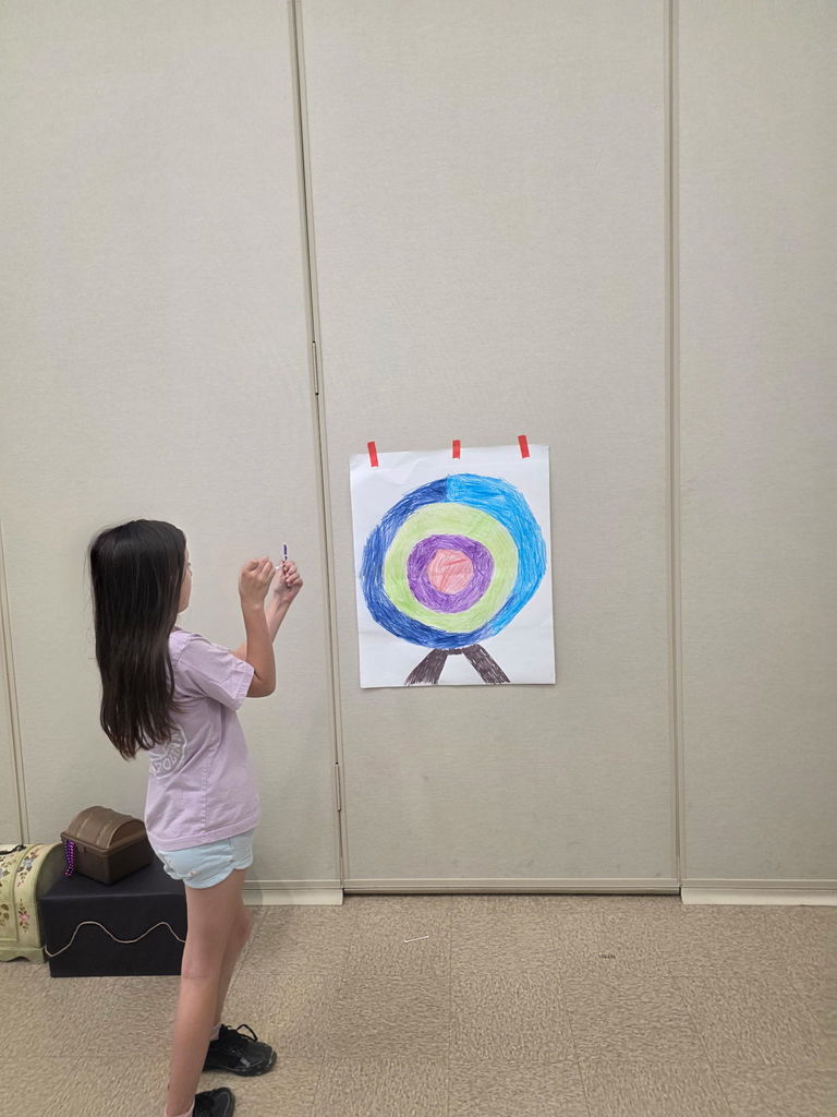 A young girl at Wildlight Elementary aiming a projectile at a colorful bullseye target mounted on a wall during Storybook STEAM Night.
