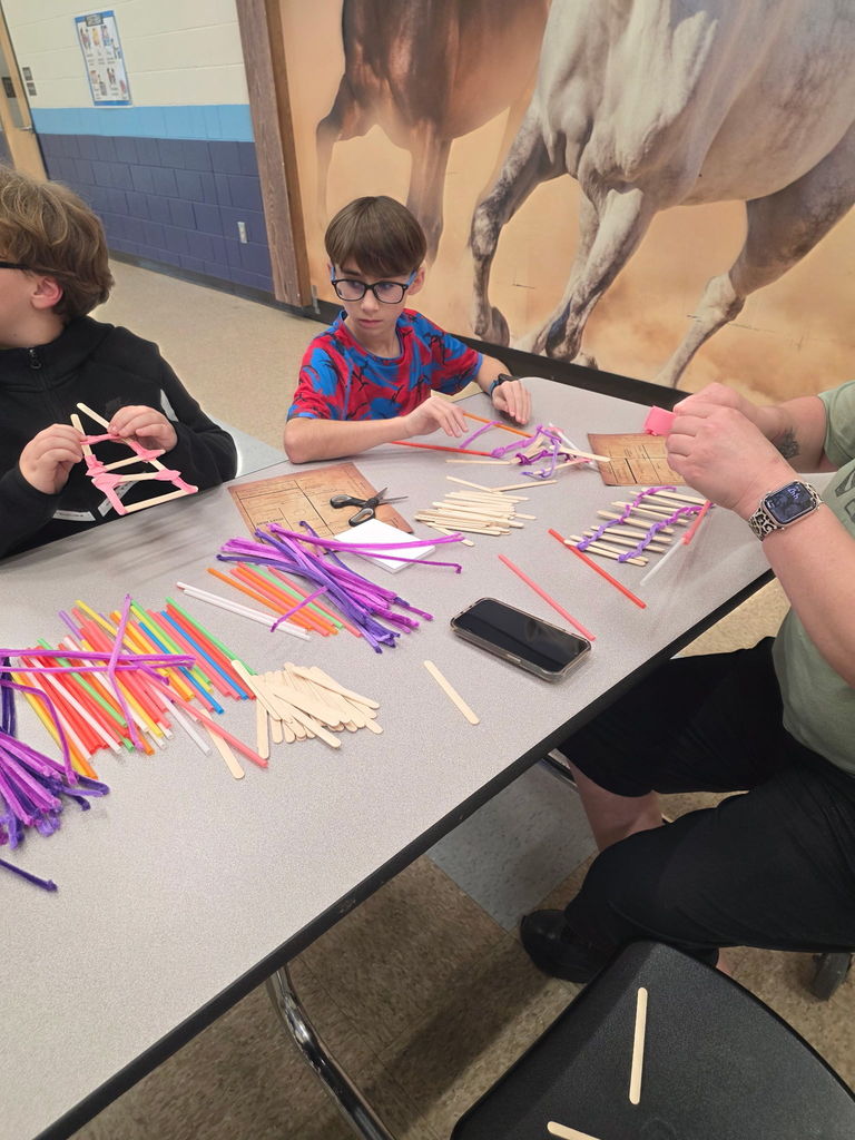 Two students and an adult collaborator sitting at a table filled with a large variety of colorful pipe cleaners and wooden sticks during Storybook STEAM Night.