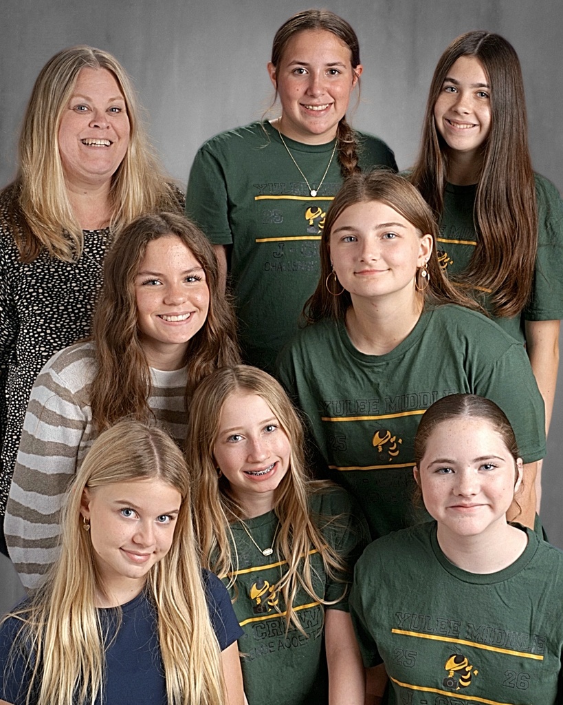 Student journalists and their teacher smile for the camera in a professional photo with a gray background. 