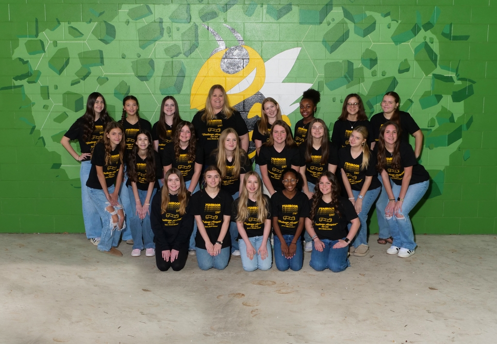 Student journalists pose in front of a green background with a yellow hornet mural painted behind them. 
