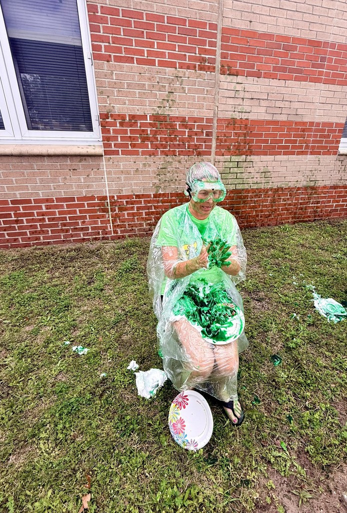 Ms. Trammell sitting in a chair full of slime and just got pied with shaving cream.