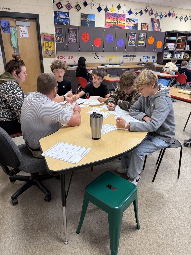 Students collaborate in small groups during a pre-algebra lesson as they complete transformation activities and record answers on worksheets.