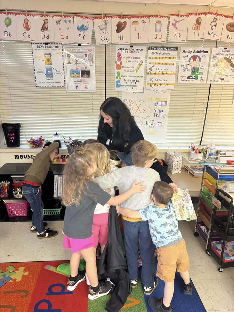 Young students gather around a teacher in a classroom at Yulee Primary School as they participate in a reading activity with visiting high school student leaders.
