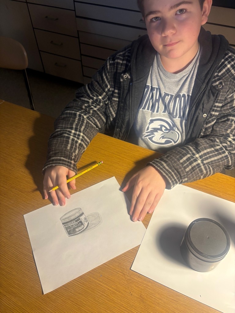 Student shows off his drawing under a lamp on a brown desk. 