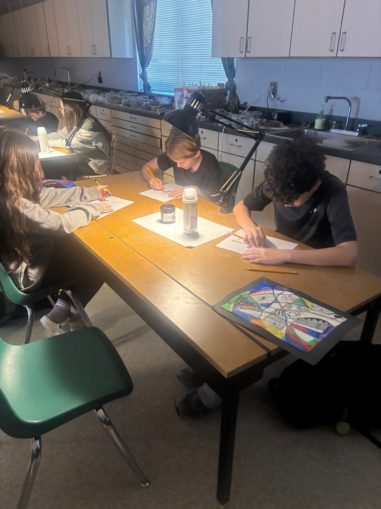 Students are shown working on their drawings using a light to show shadows. 