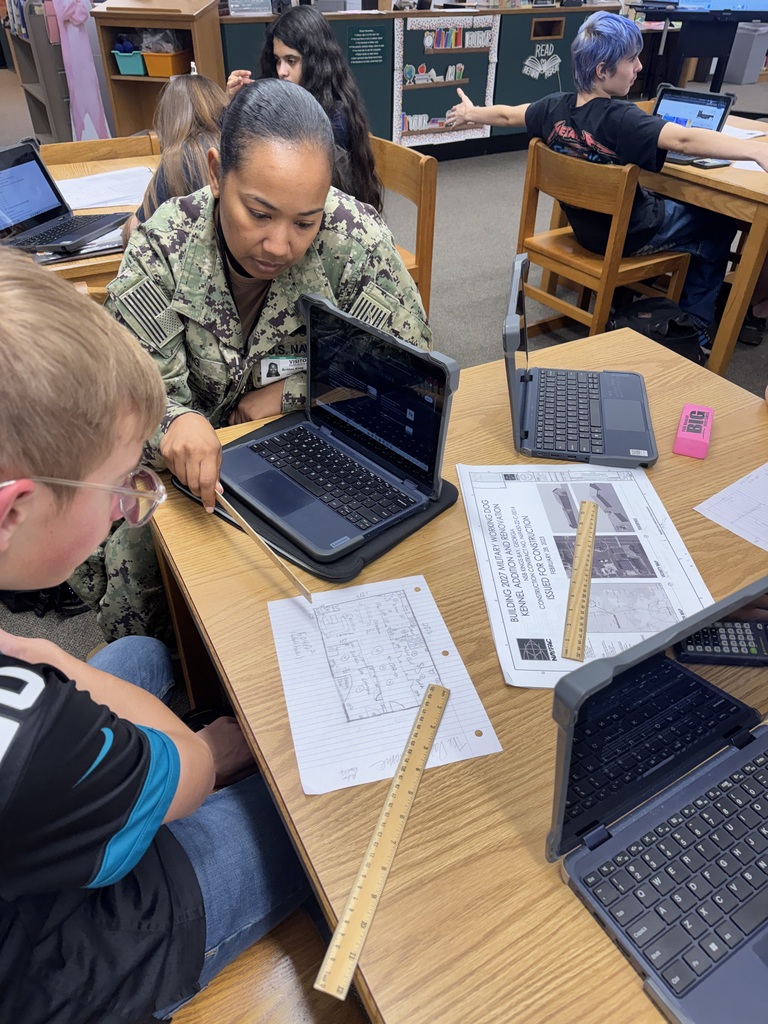 Mrs. King works with students on their blue prints in the library at their table. 