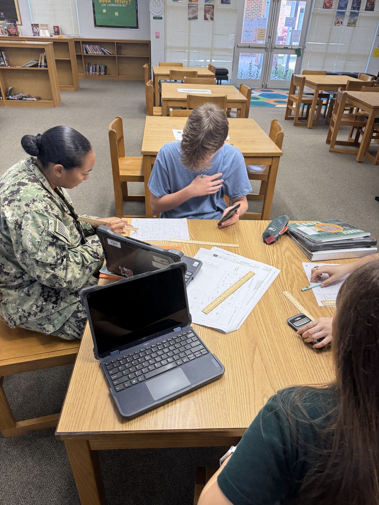 Speaker in military uniform works alongside students at their table in the library. 