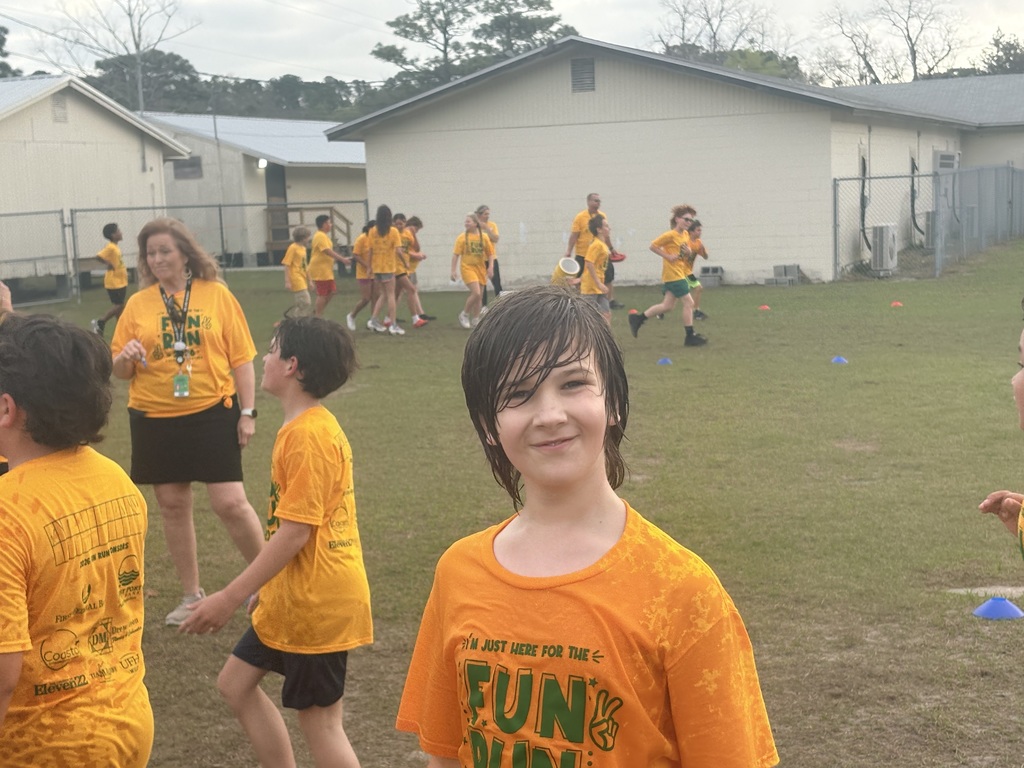 A group of elementary students in matching yellow Hornet t-shirts running across a grass field during a sunny outdoor school fundraiser.