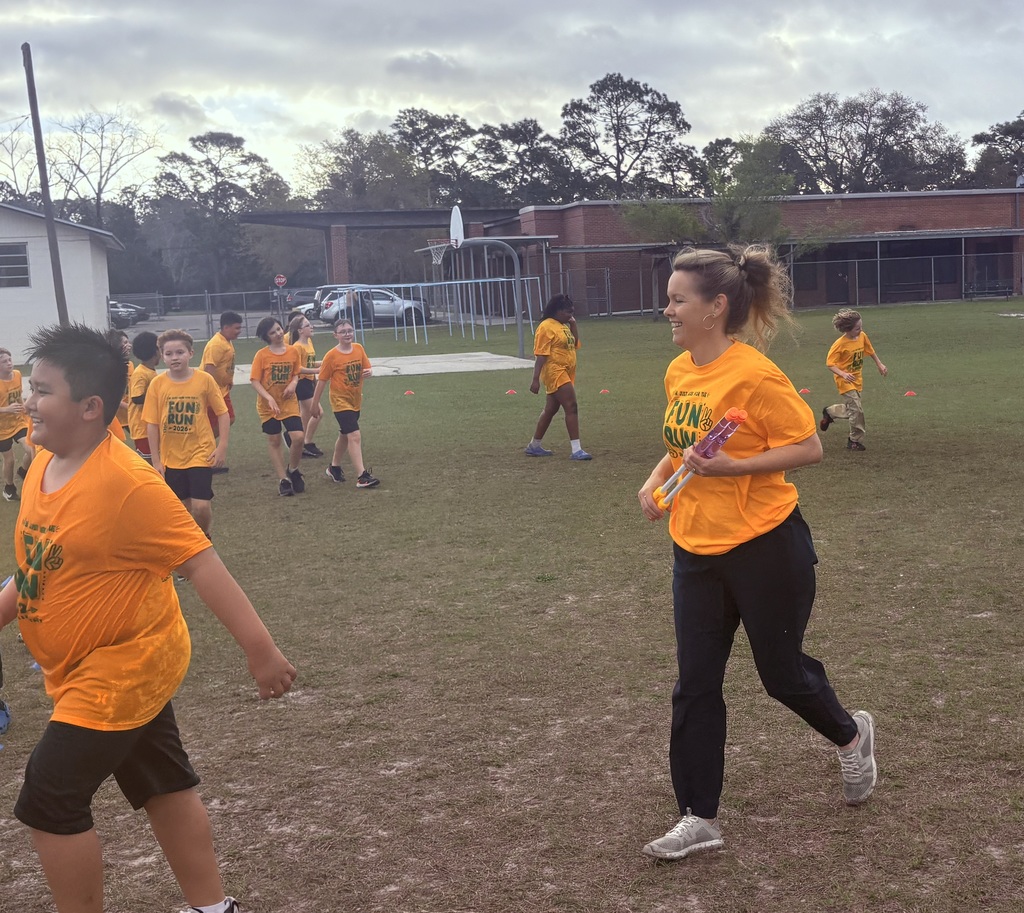 A group of elementary students in matching yellow Hornet t-shirts running across a grass field during a sunny outdoor school fundraiser.
