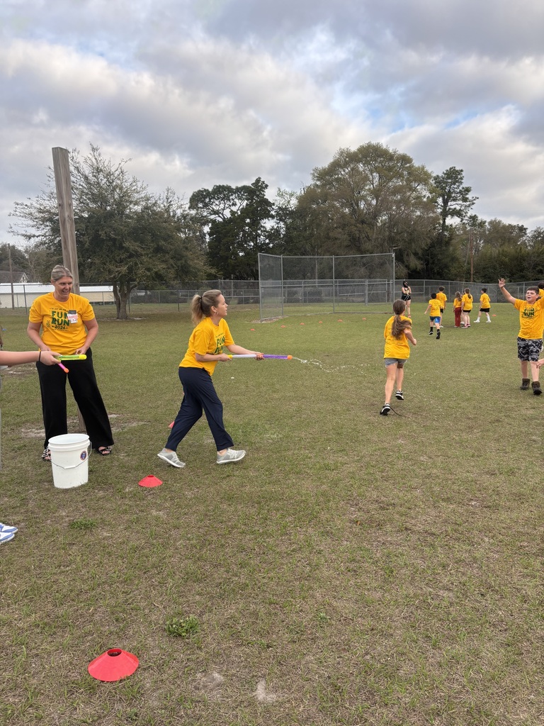 School staff and volunteers standing by water buckets, spraying students as they run past during the fundraiser.