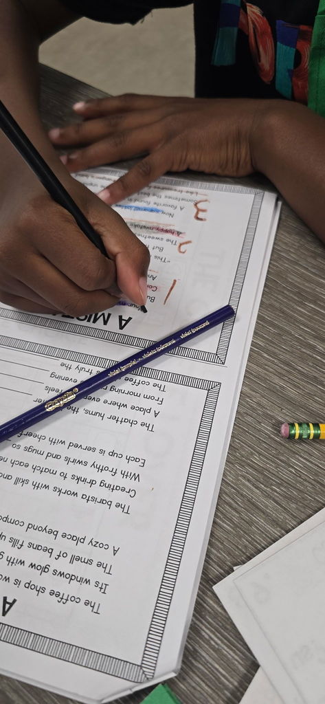 Close-up of a student's hand writing a poem on a specialized "Starbucks Poetry" worksheet, showing the creative process in action.