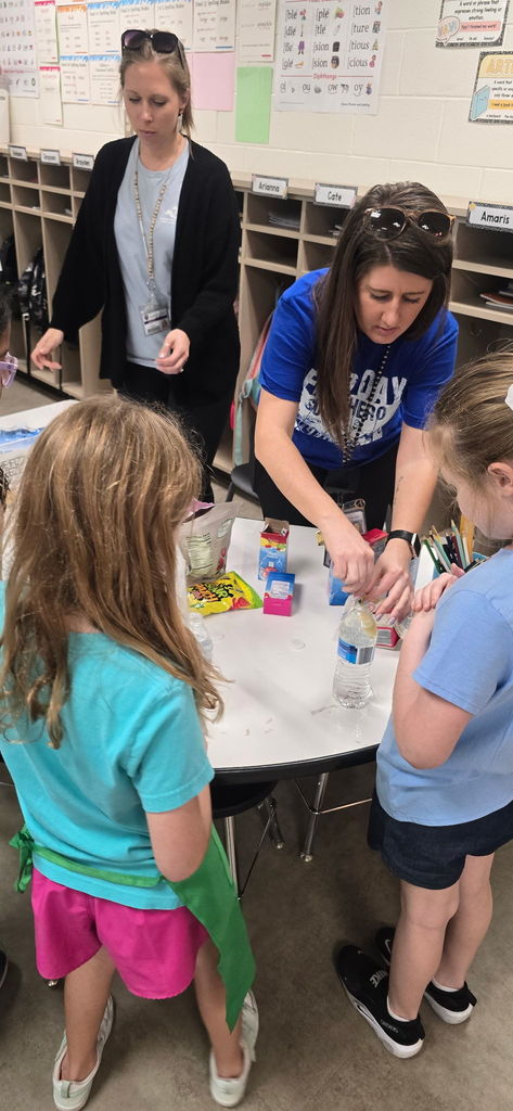 Two adults at Wildlight Elementary assist a group of 2nd-grade students at a table as they mix and pour ingredients to create their "refreshing reward" drinks during Starbucks-themed Poetry Week.