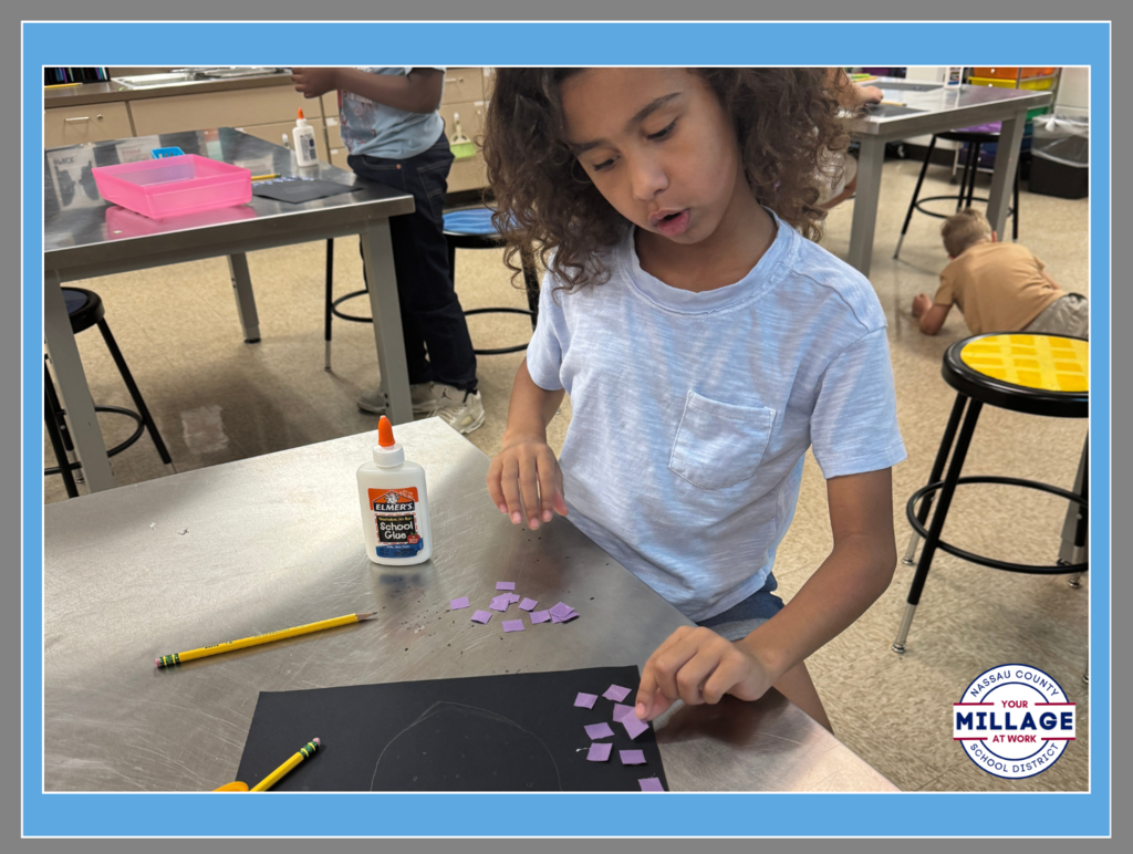 A student at Wildlight Elementary carefully gluing small purple paper squares onto a black background for an art project.