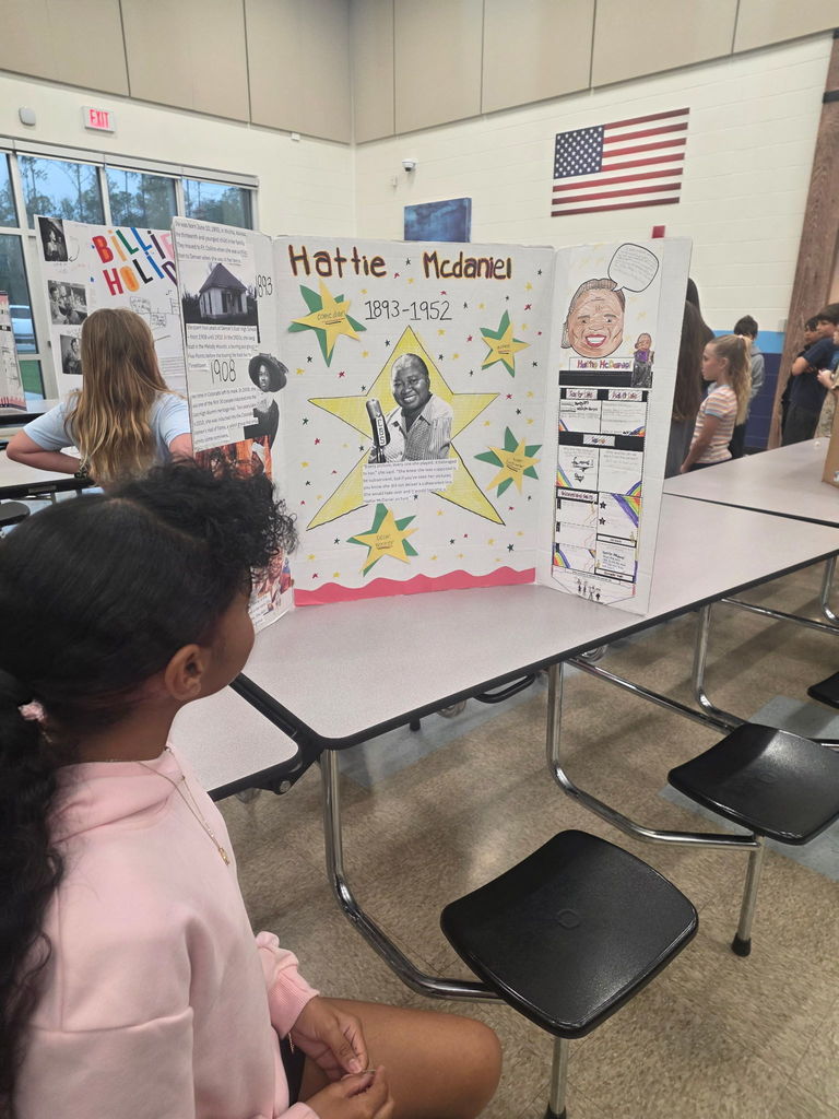 A young student at Wildlight Elementary looks at a Living Museum display board about Hattie McDaniel, which features biographical facts and a printed portrait of the actress.