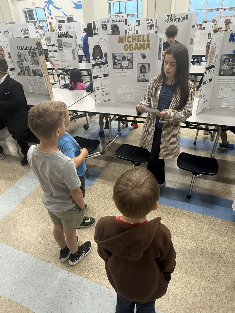 A 4th-grade student at Wildlight Elementary uses a pointer to present her "Living Museum" display about Michelle Obama to two younger students.