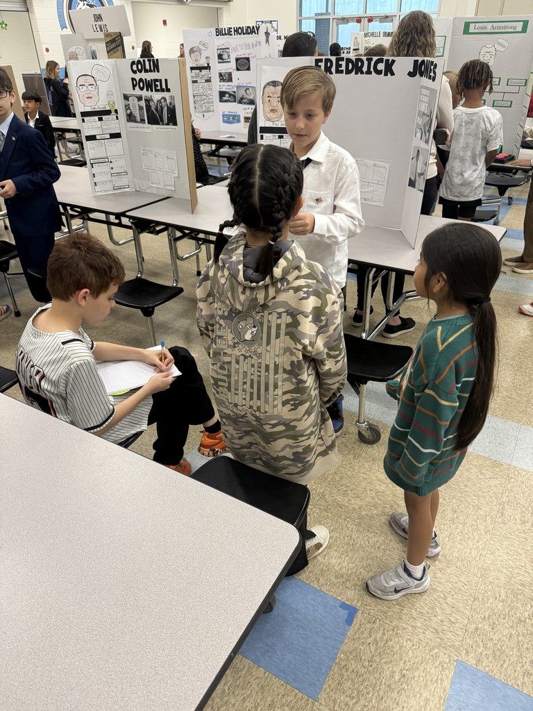 A 4th-grade student at Wildlight Elementary stands by their "Living Museum" display about Fredrick Jones, explaining their research to a group of younger students.