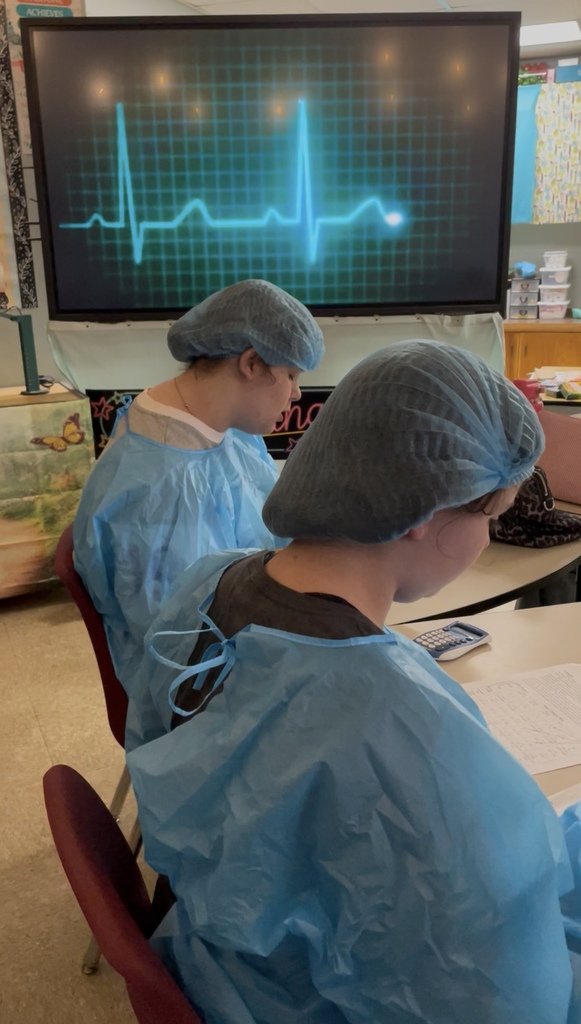 Students dressed in hospital scurbs working at their desk.